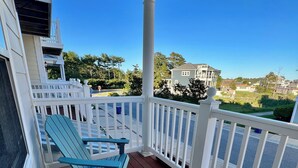 Un espacio al aire libre cubierto con sillas Adirondack, barandal blanco y vista a casas y árboles.