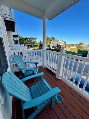 A covered outdoor area with Adirondack chairs, a white railing, and a view of houses and trees. - Bay access, boat slip, pool, sleeps 12, pet friendly and near the beach.   (Ocean View)