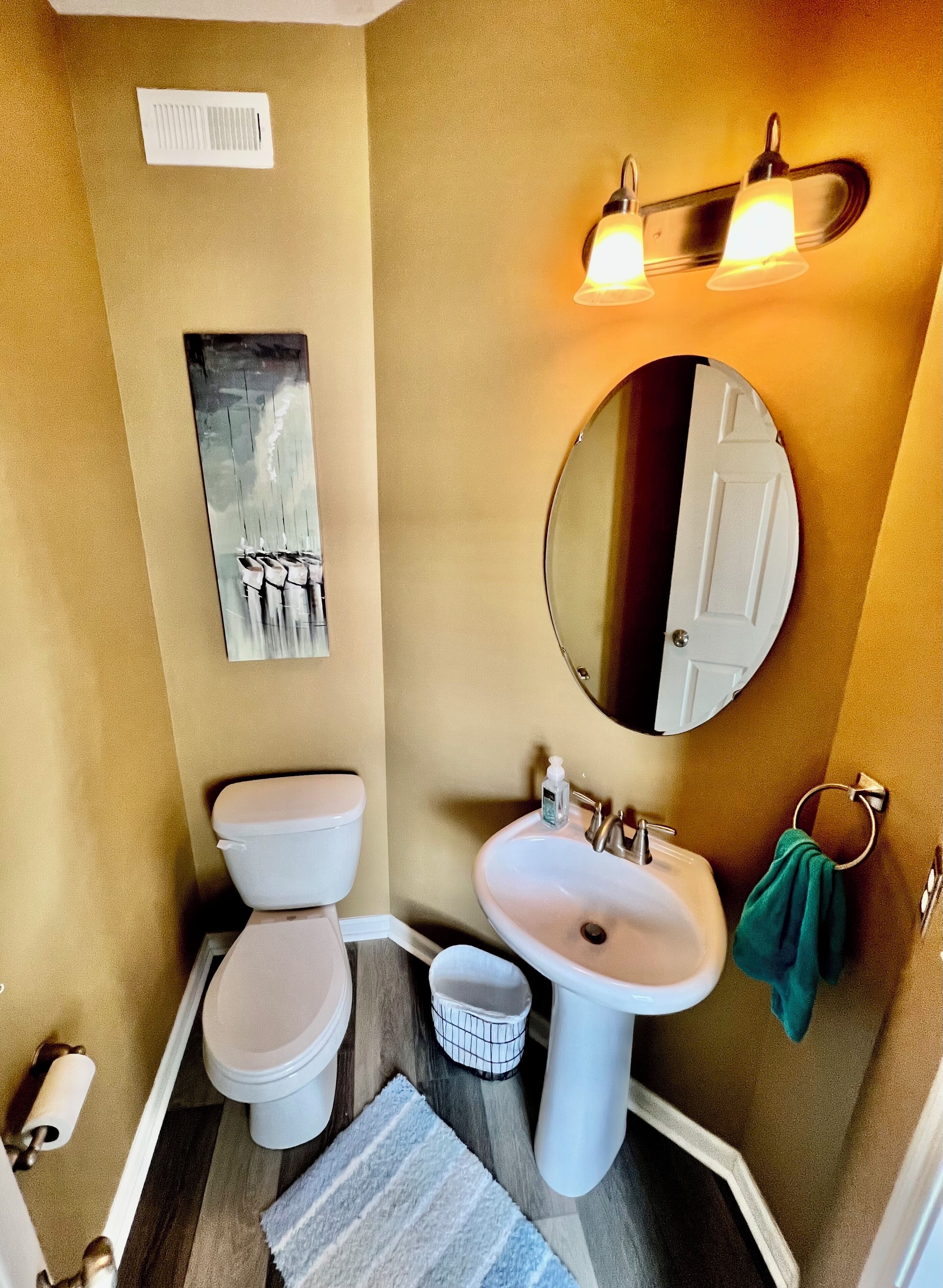 A bathroom with a toilet, sink, mirror, and a wall-mounted light fixture.