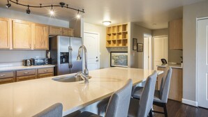 Une cuisine moderne avec des meubles en bois, un réfrigérateur en acier inoxydable, un four encastré et un grand îlot central doté de tabourets de bar.