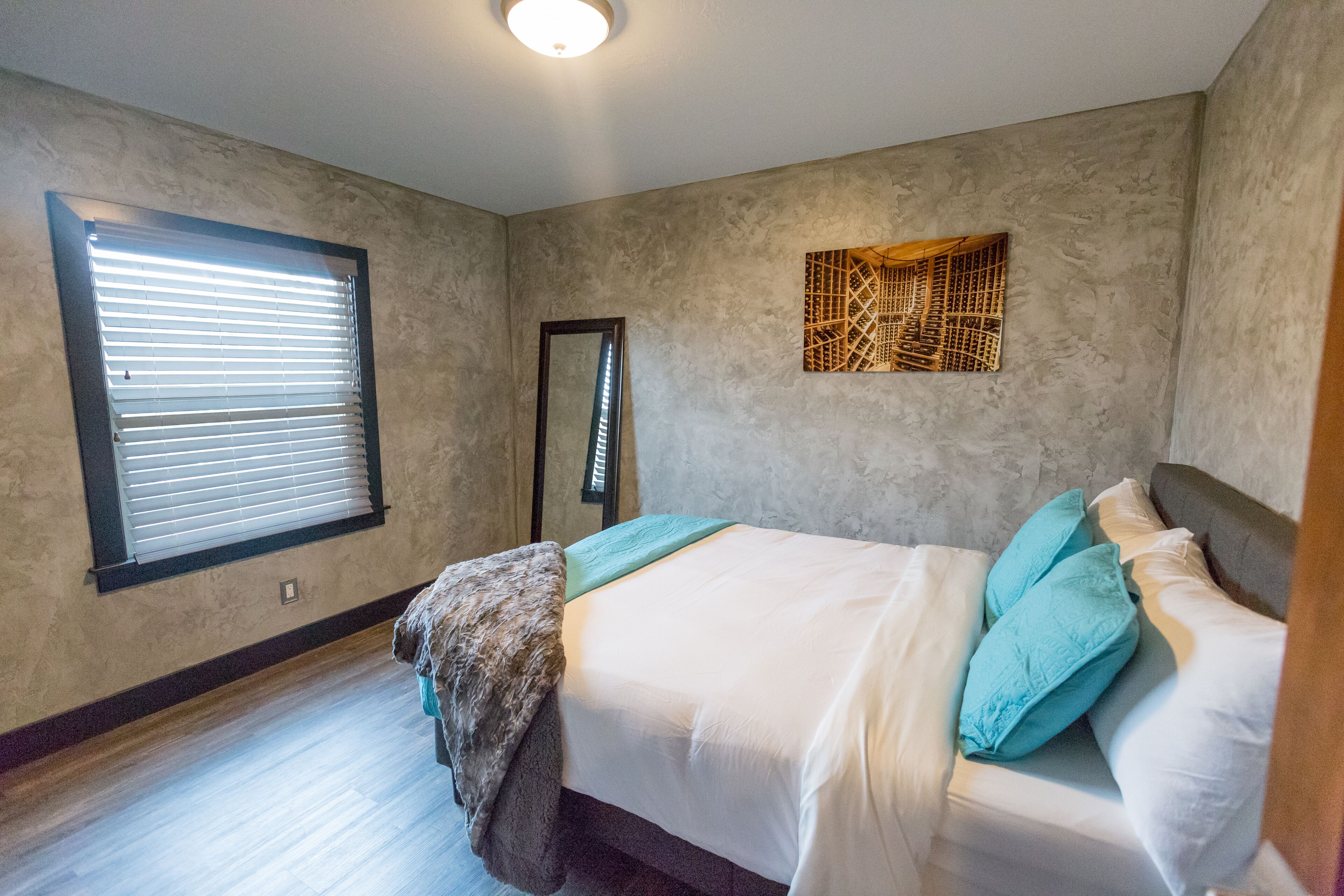 A bedroom with a bed, a window with blinds, a door, and a textured wall decoration.