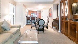 A living room with a sofa, coffee table, dining table with chairs, kitchen area, and a TV on a wooden cabinet.