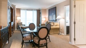 A hotel room with a dining area, a sofa, a lamp, and a painting on the wall.