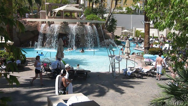 A pool area with a waterfall feature, lounge chairs, and palm trees.