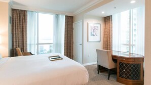 A hotel room with a large bed, a desk, and a chair. There are curtains on the windows, and a framed picture on the wall.