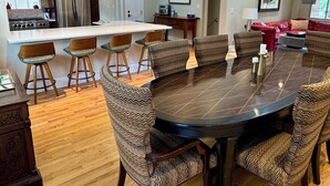 Un'ampia zona pranzo con un tavolo rotondo grande e sei sedie, una cucina con elettrodomestici moderni e un divano rosso nella sala giorno.