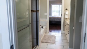 A narrow bathroom with a shower, a bathtub, and a toilet. There is a small rug in front of the bathtub.