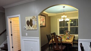 A dining area with a table set for four, a chandelier, and a window with blinds.