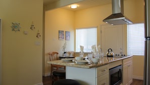 A kitchen with a central island, white cabinets, a stainless steel range hood, and a window with blinds. - Premium Coastal Getaway: A Seaside Retreat Unit G  (Carlsbad)