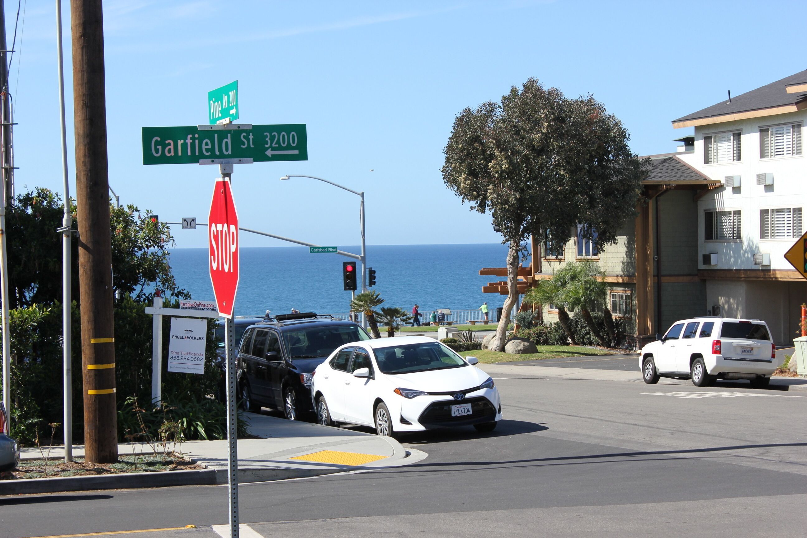 A street intersection with a stop sign, street signs for Garfield St and Carlsbad Blvd, and a view of the ocean in the background.