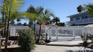 A pool area with a white fence, palm trees, and a building in the background. - Premium Coastal Getaway: A Seaside Retreat Unit G  (Carlsbad)