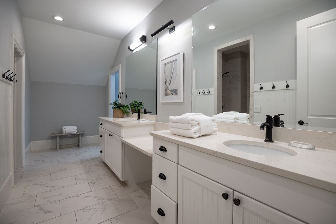 A modern bathroom with a large mirror, two sinks, and a bench.