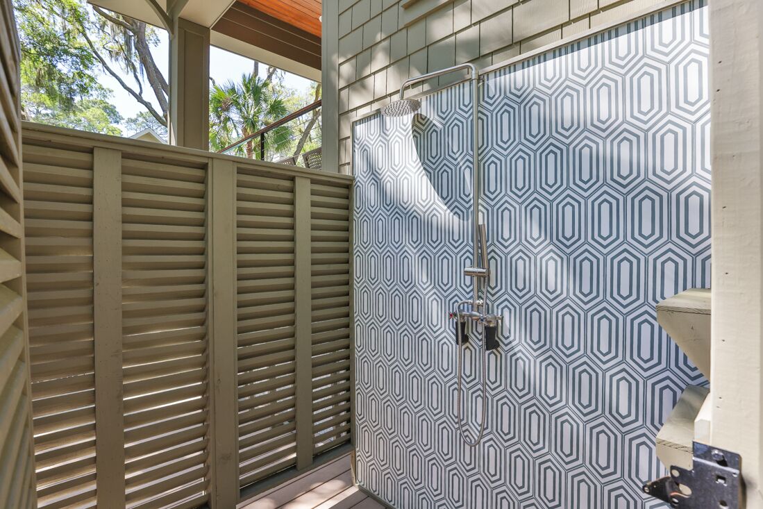Ein Badezimmer mit einer Dusche, deren Wand ein geometrisches Muster aufweist, und einer Holztür.