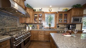 A kitchen with wooden cabinets, a stainless steel stove, granite countertops, and a window with a view of trees.