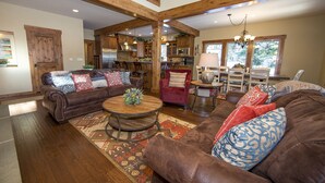 A spacious living room with a high ceiling and exposed wooden beams, furnished with leather sofas and a central coffee table.