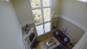 A living room with a brown leather sofa, a coffee table, and a TV on a stand. There is a large window with blinds, and a small table with a lamp. - Desert Sky, Eagle Crest Home. Golf on site, close to pool (Redmond)