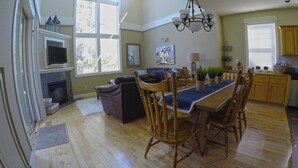 A spacious living area with a dining table, chairs, a fireplace, and a large window providing natural light. - Desert Sky, Eagle Crest Home. Golf on site, close to pool (Redmond)