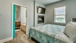 A bedroom with a bed, a TV mounted on the wall, a window with blinds, and a door leading to a bathroom. - LARGE HOME w HUGE KITCHEN sleeps 50+huge pool+cinema+game room 1min to the SAND (North Myrtle Beach)