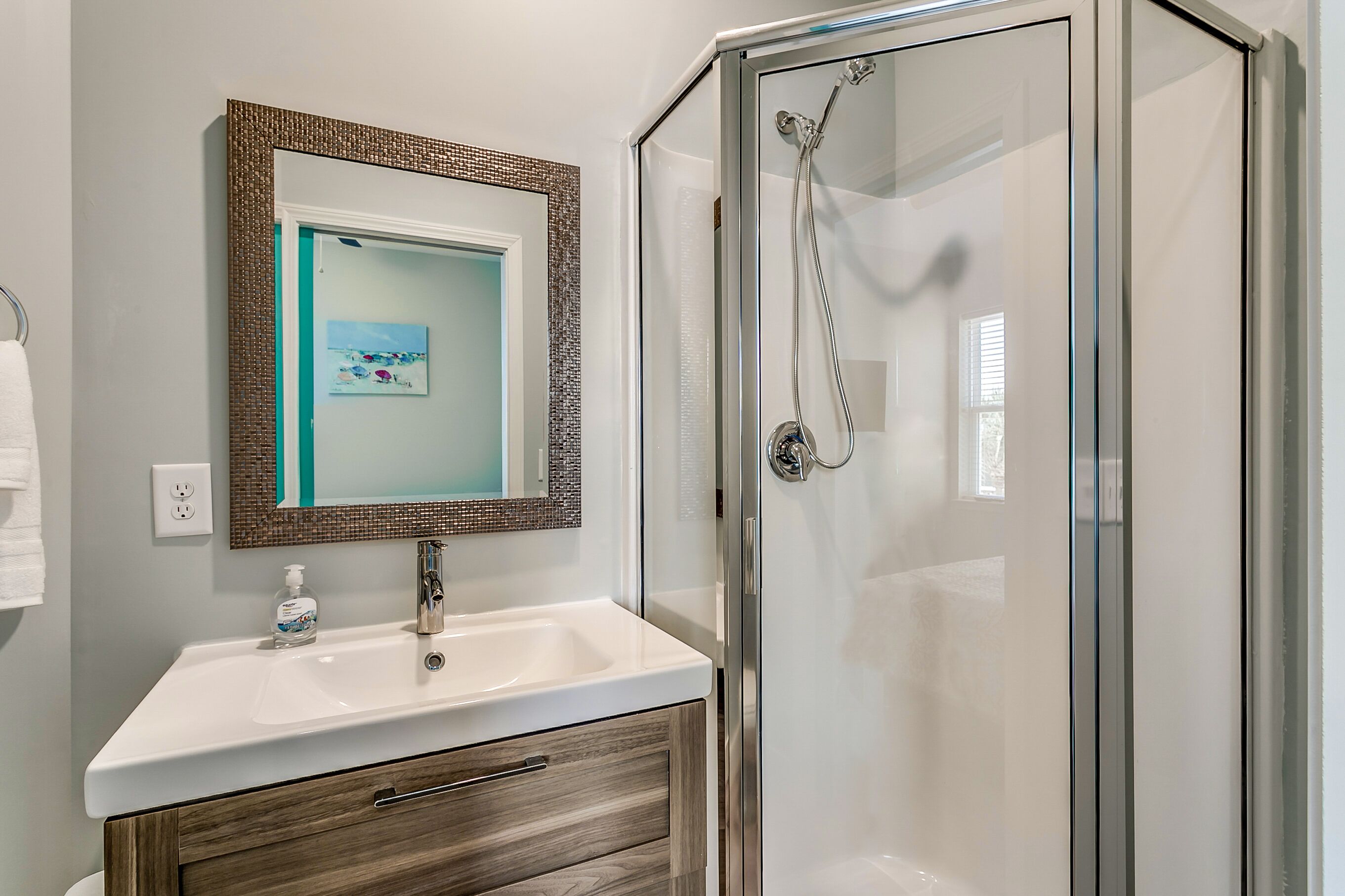 Un baño con lavamanos blanco, mueble de madera y cabina de ducha de vidrio.