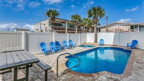 A swimming pool with blue chairs and a table, surrounded by a white fence and palm trees. - LARGE HOME w HUGE KITCHEN sleeps 50+huge pool+cinema+game room 1min to the SAND (North Myrtle Beach)