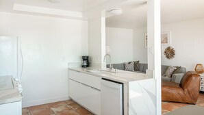 Una cocina moderna con armarios blancos, lavavajillas integrado y cafetera sobre la encimera.
