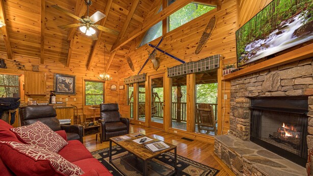 A cozy cabin interior with a stone fireplace, wooden ceiling, and large windows. - Perfect location, Secluded, Pet Friendly, Wooded Paradise (Sevierville)
