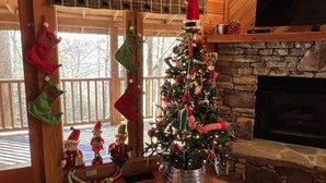 A cozy cabin interior with a decorated Christmas tree, wooden walls, a stone fireplace, and festive stockings. - Perfect location, Secluded, Pet Friendly, Wooded Paradise (Sevierville)