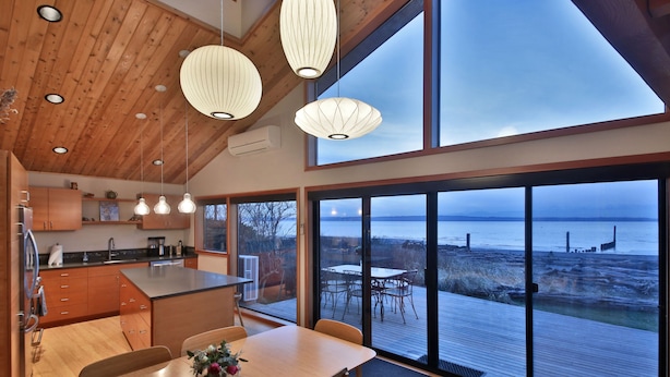 Een moderne keuken met houten kasten, een centraal eiland, hanglampen en grote ramen met uitzicht op de zee.