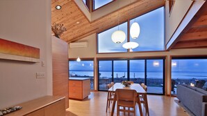 Een modern interieur met een eethoek, houten meubels en grote ramen met uitzicht op zee.
