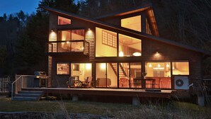 Een houten vakantiehuis met meerdere verdiepingen, grote glasramen, een terras en een trap naar de hogere etages.