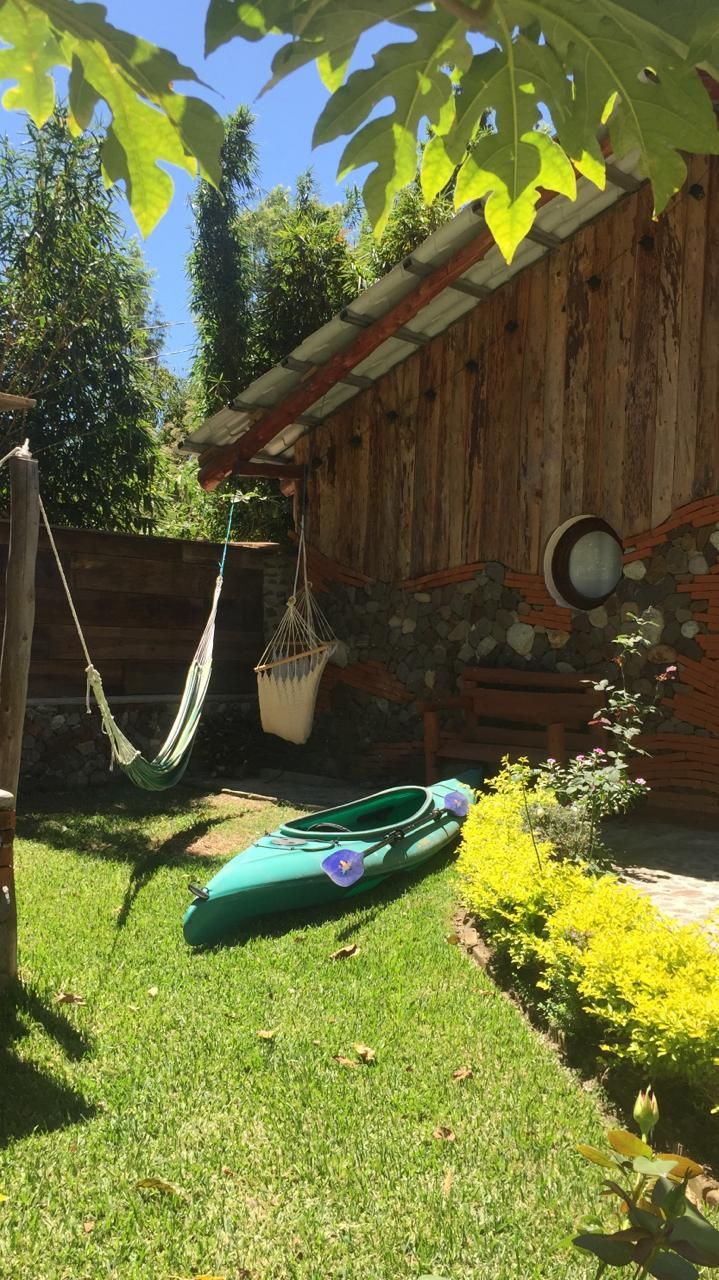 A wooden structure with a stone wall, a hammock, a green kayak, and yellow flowering plants.