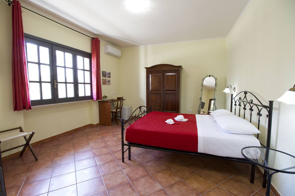 A bedroom with a bed, a desk, a chair, and a window with curtains.