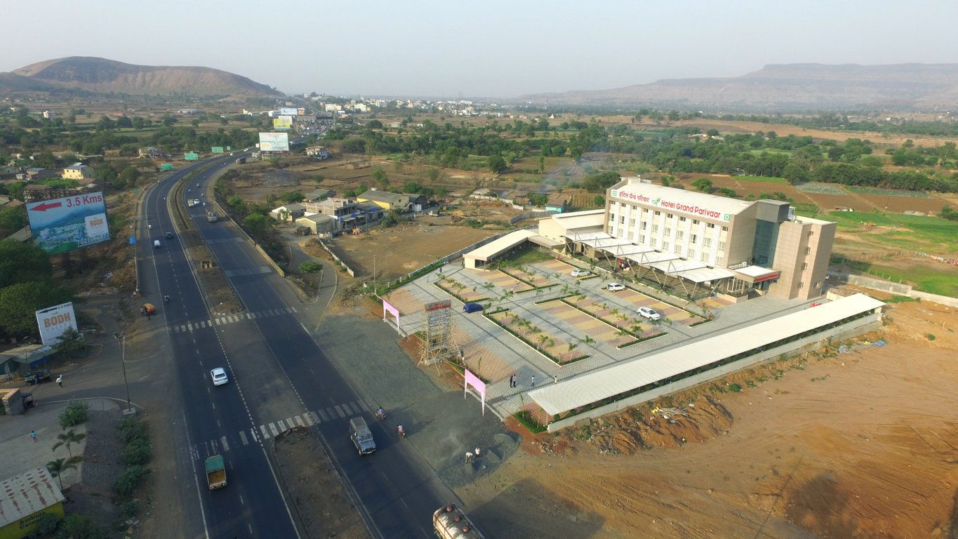 A large hotel with a flat roof and multiple floors, surrounded by a parking lot and a highway.