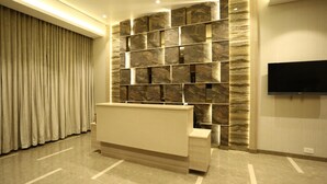 Un área de recepción con pared de mármol, una televisión de pantalla plana y una cortina.