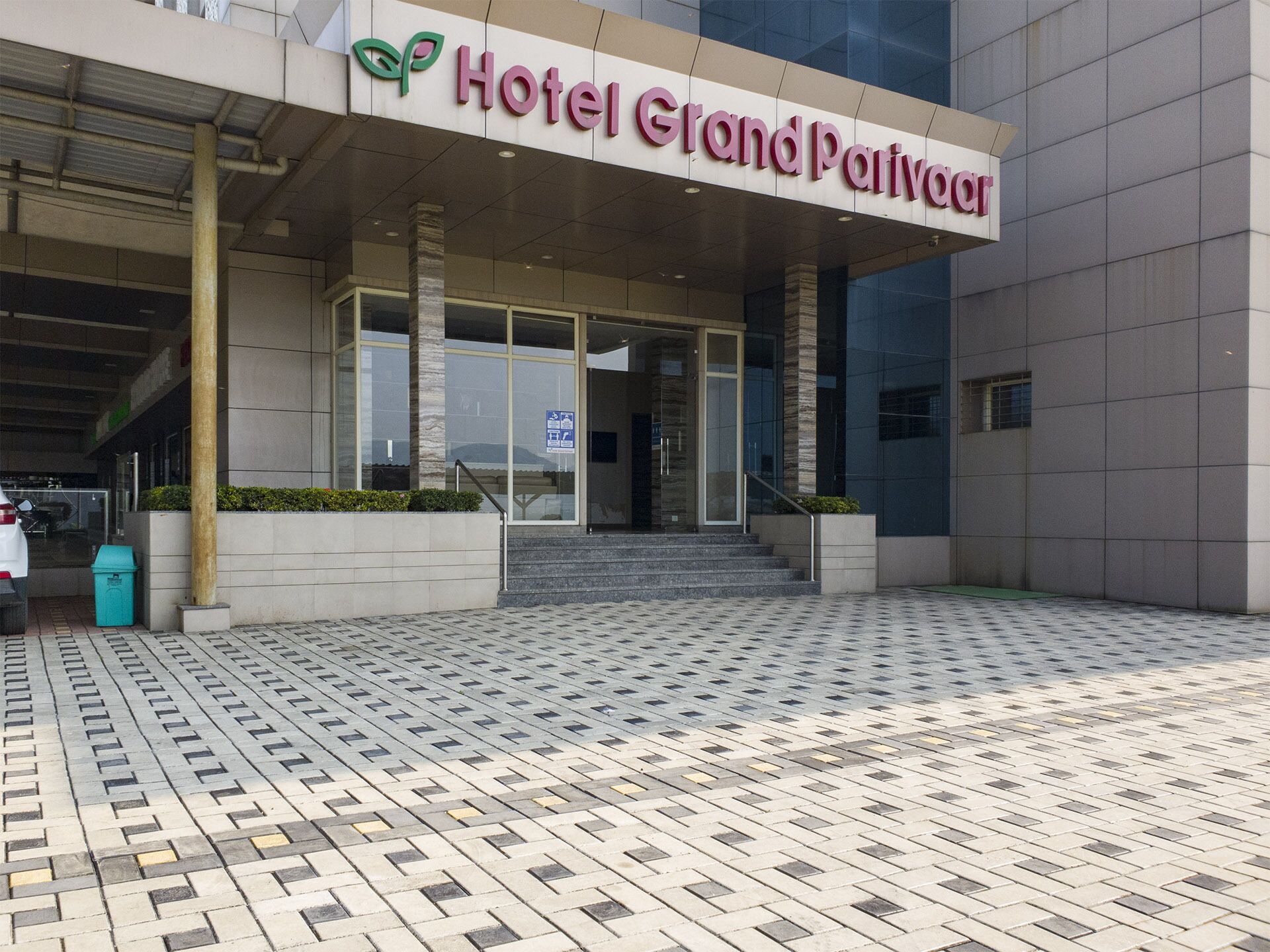 La entrada del Hotel Grand Parivar, con suelo de baldosas y una vista despejada de las puertas de acceso.