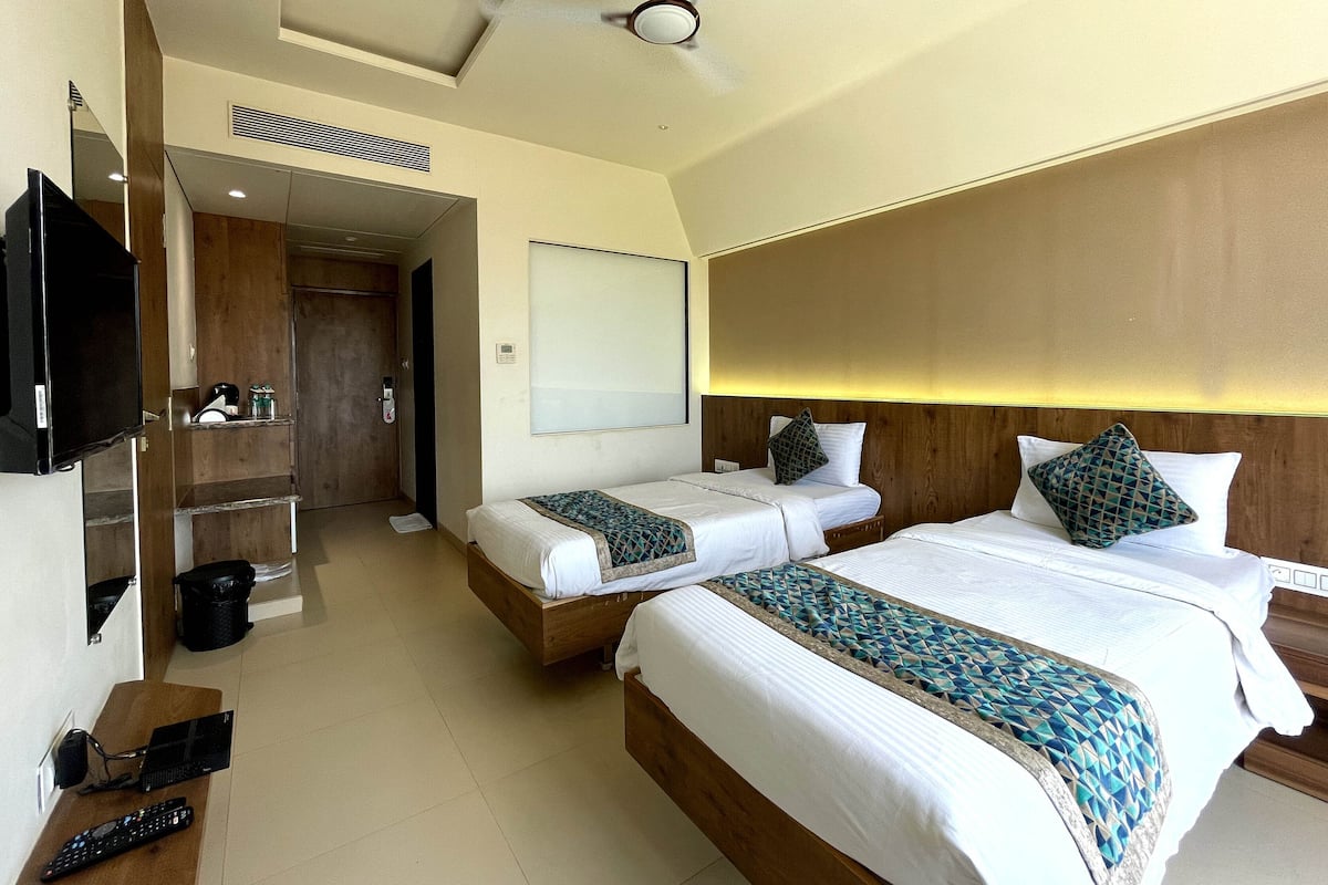 A hotel room with two beds, a TV, a desk with a laptop, and a ceiling fan.