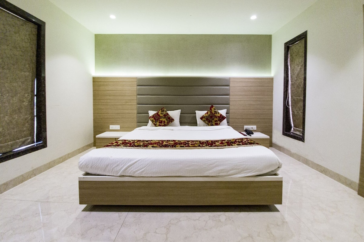 A modern hotel room with a large bed, a headboard with horizontal panels, bedside tables, and framed artwork on the walls.
