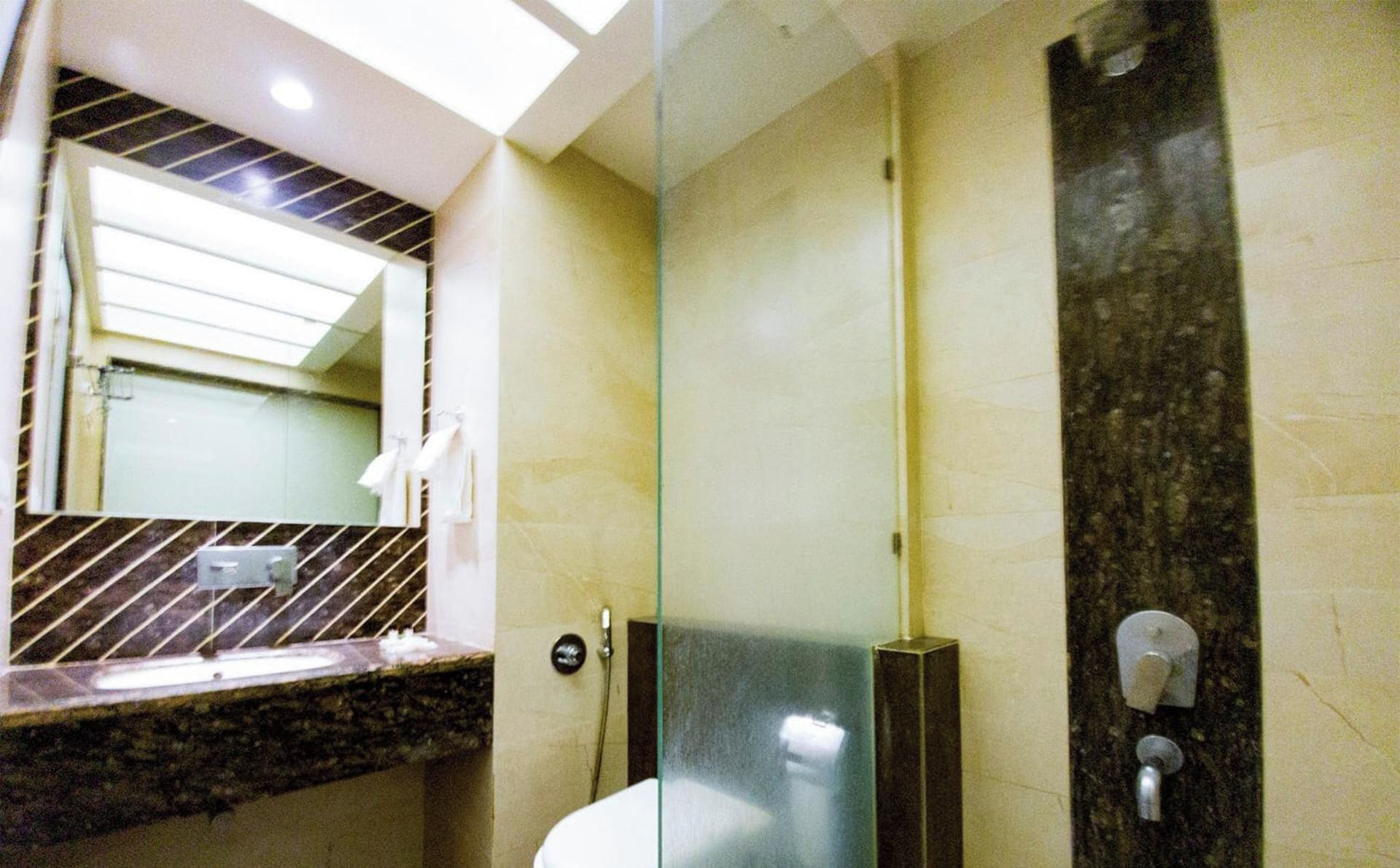 A bathroom with a glass shower enclosure, a marble countertop, and a mirror above the sink.