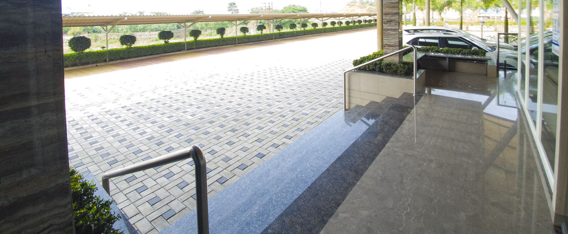 A modern hotel entrance with a tiled pathway leading to a covered area with a car parked nearby.