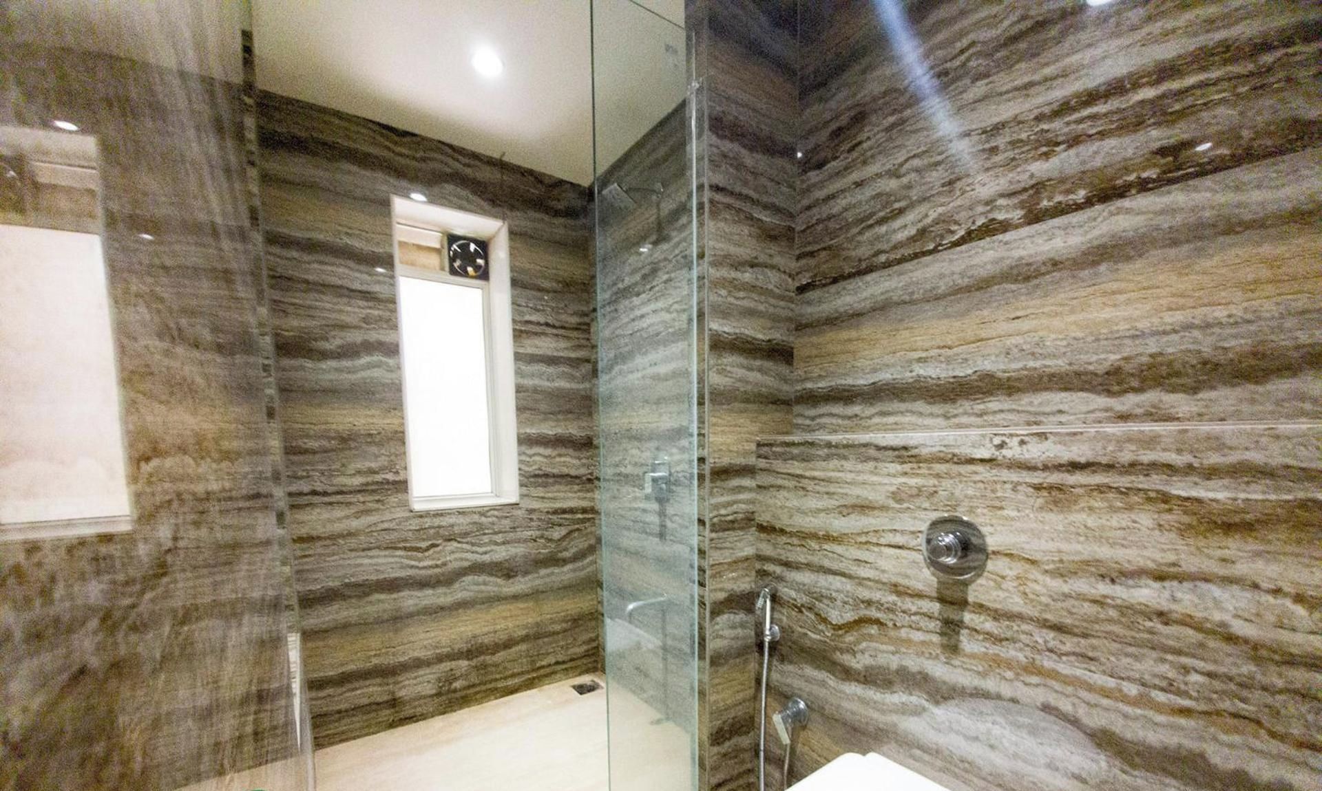 A modern bathroom with a glass shower enclosure and a marble-patterned wall.