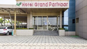 La entrada del Hotel Grand Parivar con un corredor cubierto y un coche aparcado cerca.