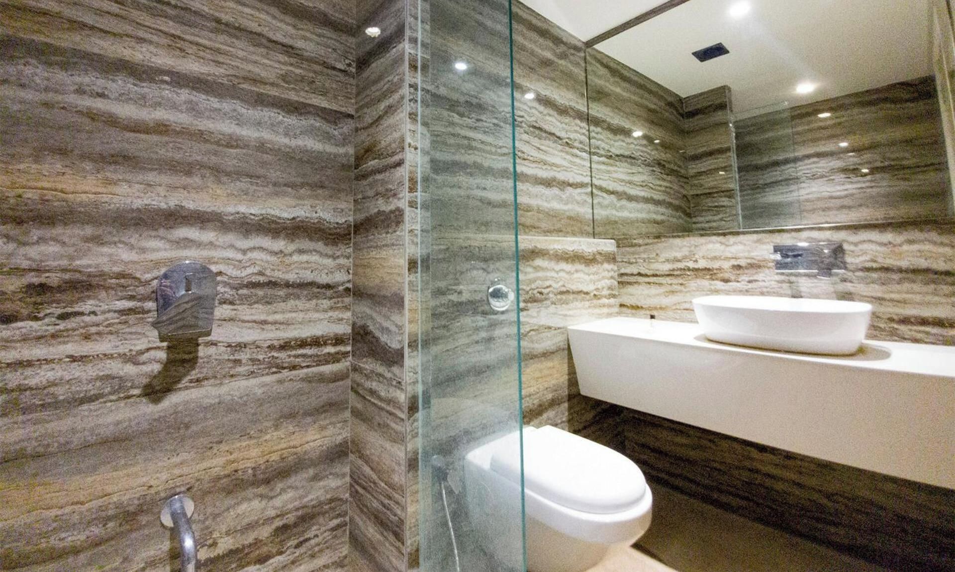 Een badkamer met een marmeren wand, een glazen douchecabine, een wit wastafelmeubel en een toilet.