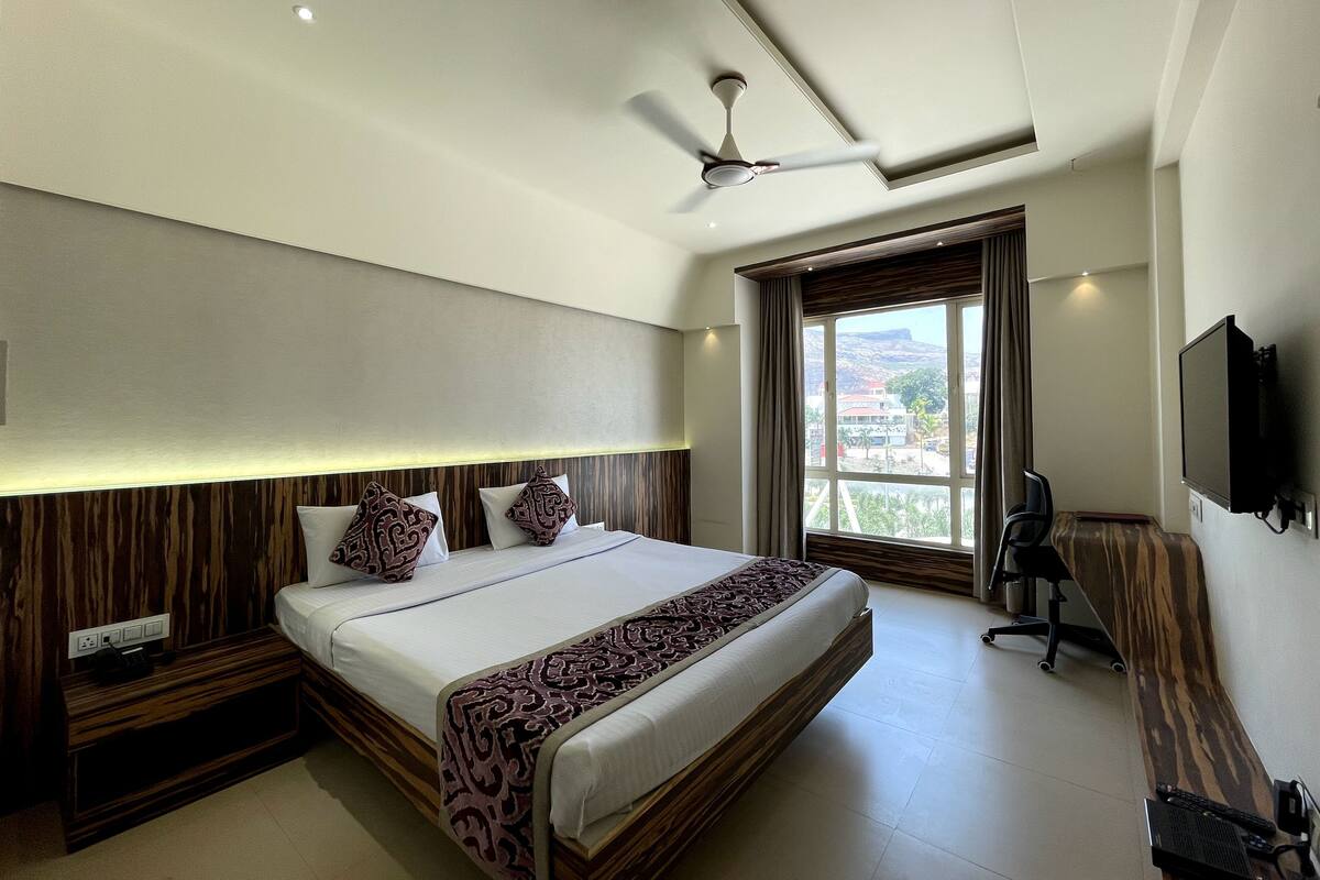 A hotel room with a large bed, a ceiling fan, a TV, and a window with a view.