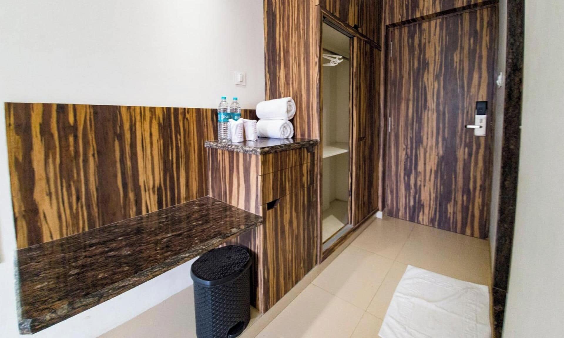 A bathroom with a wooden wall design, a towel rack, a shelf with toiletries, a trash bin, and a shower area.