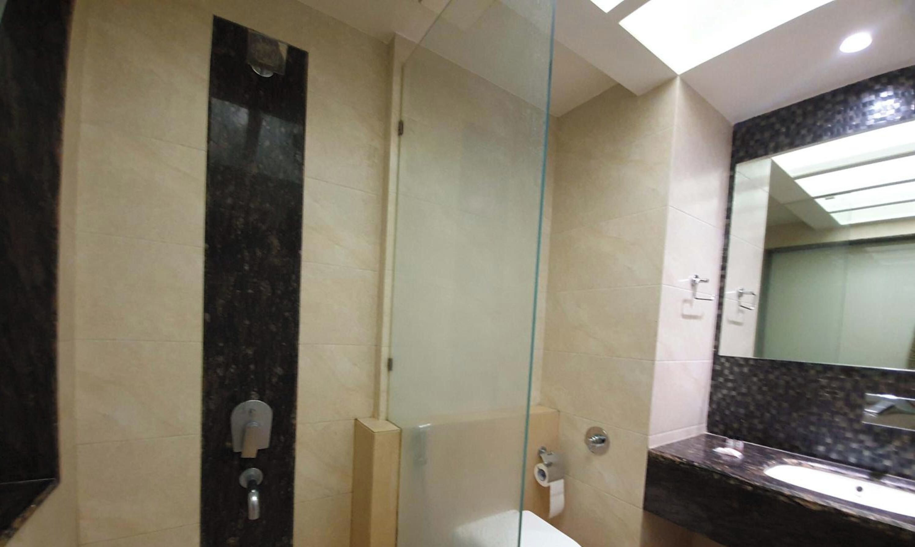 A modern bathroom with a glass partition, a marble-tiled wall, a sink, and a mirror.