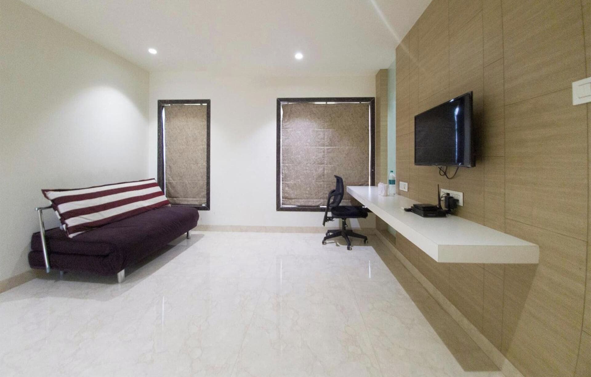 A modern office space with a sofa, a desk, and a television on the wall.