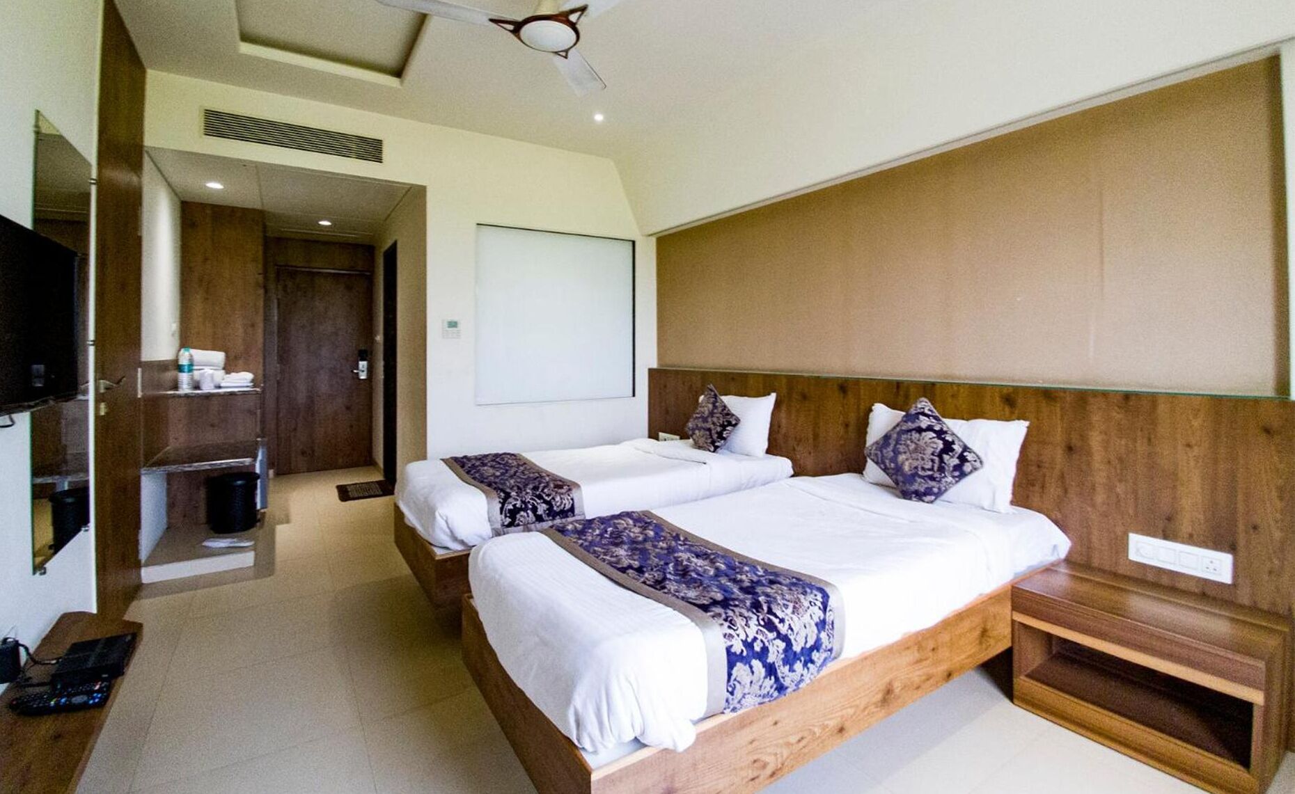 A hotel room with two beds, a TV, a wooden headboard, and a small bedside table.