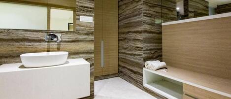 Un baño moderno con un lavamanos grande de color blanco, un espejo y una pared de mármol.