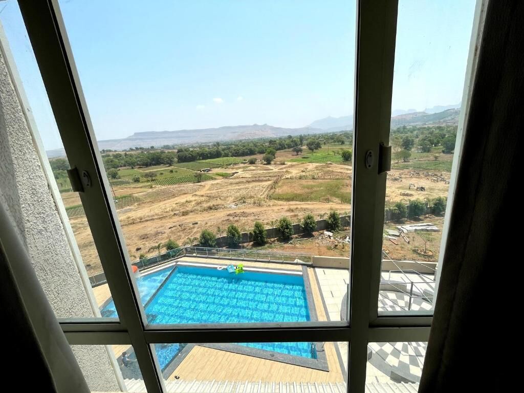A view from a window overlooking a swimming pool and a landscape with fields and distant hills.