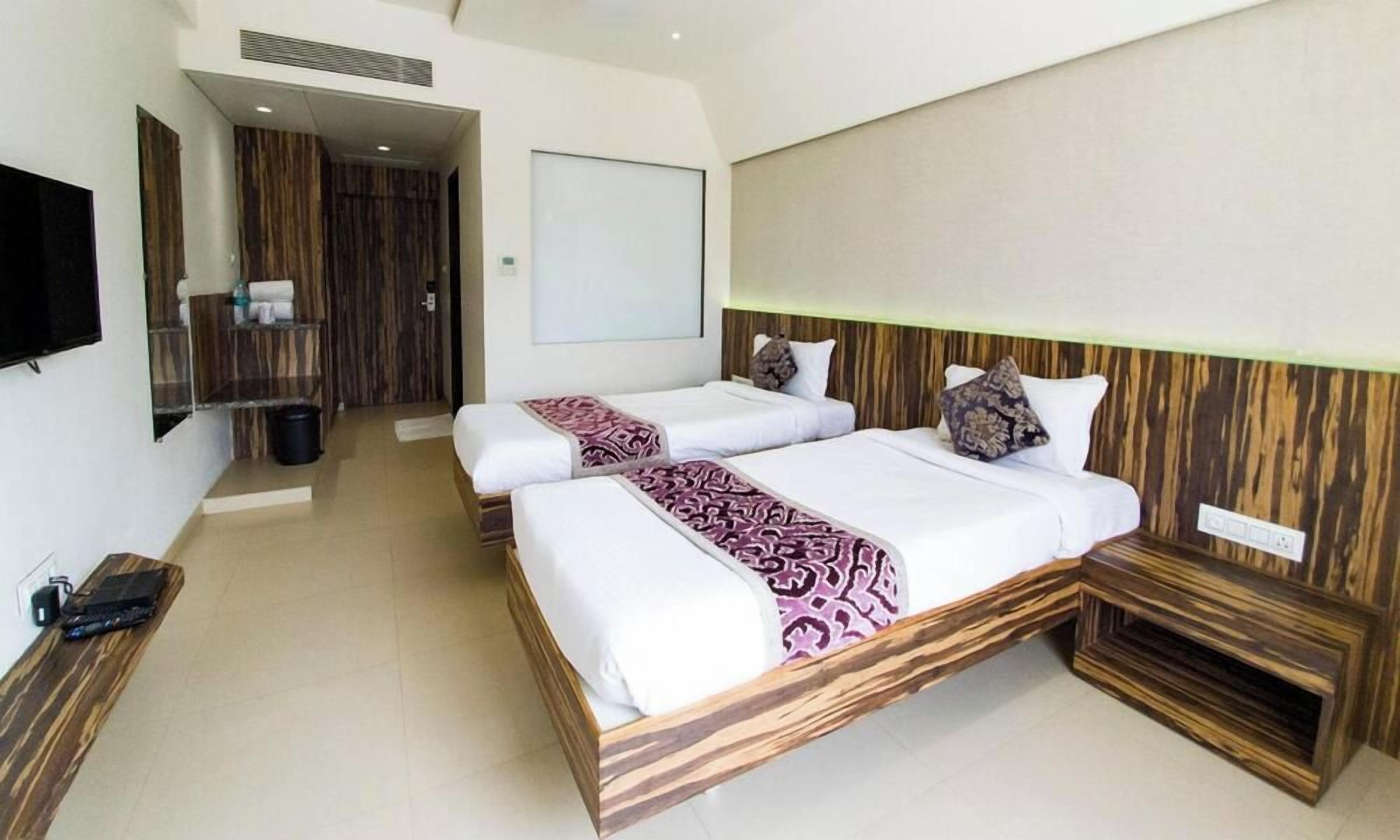 A hotel room with two beds, a television, a mirror, and a wooden headboard.